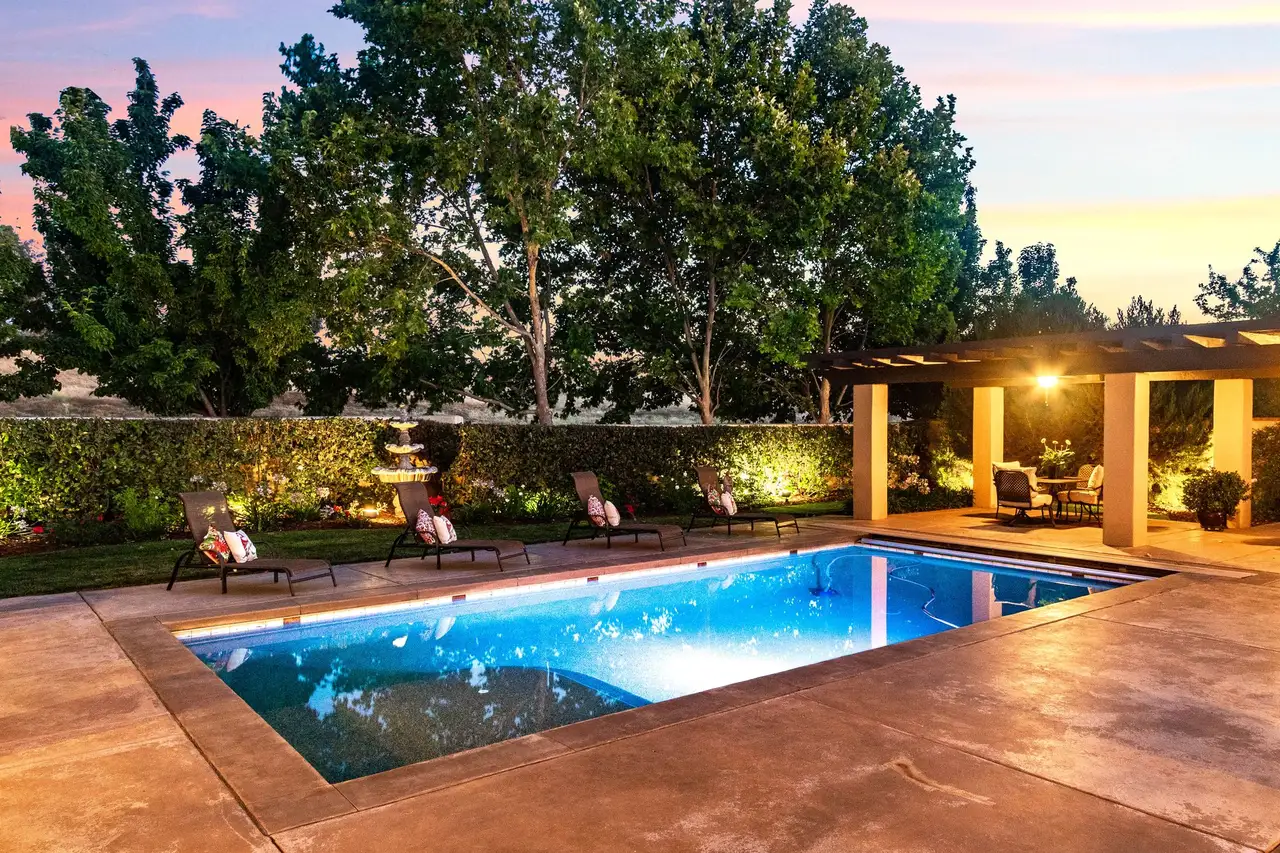 Backyard pool and cabana with landscape lighting at dusk