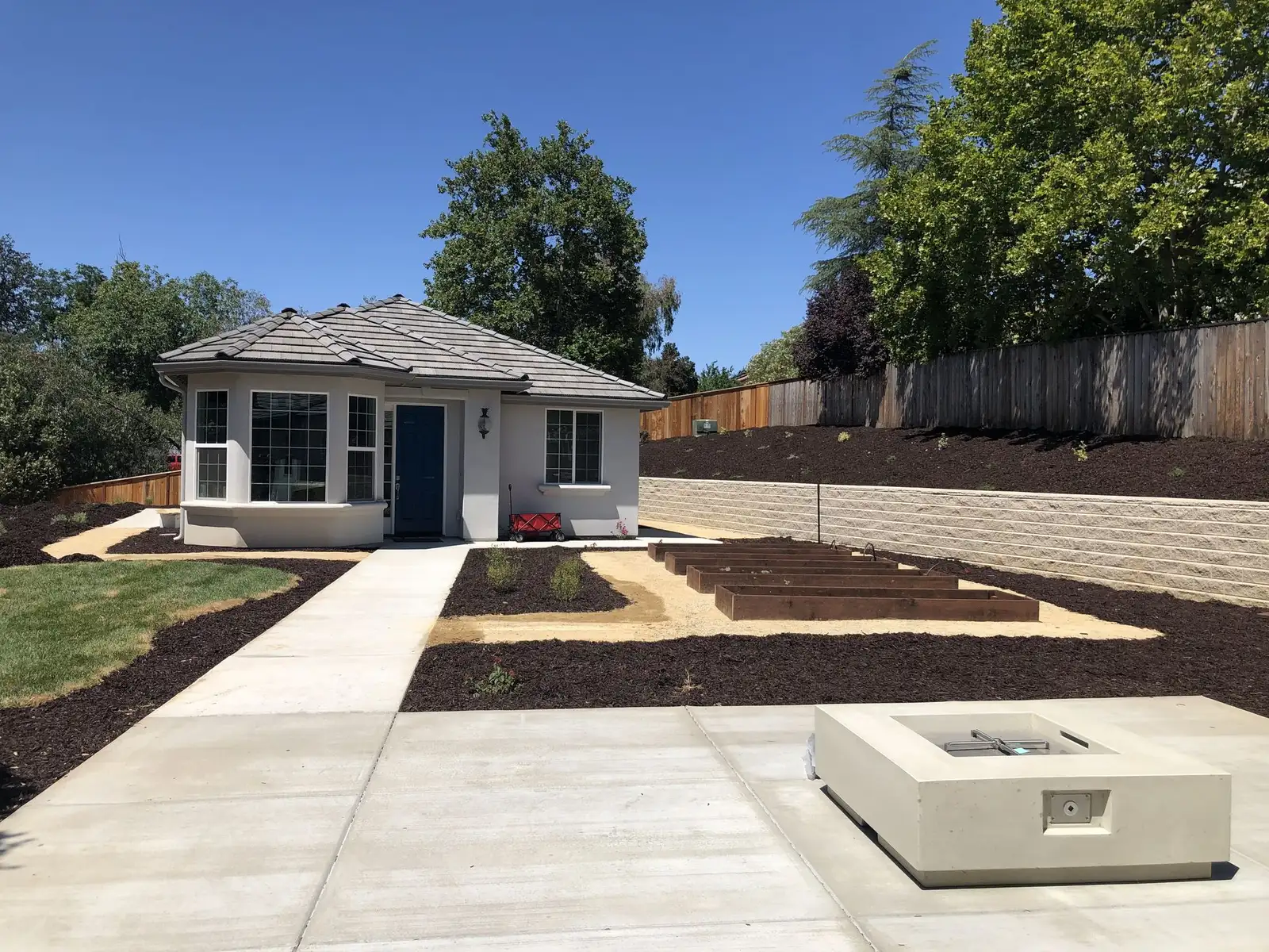 Concrete walk to a cottage with a fire bowl and raised beds