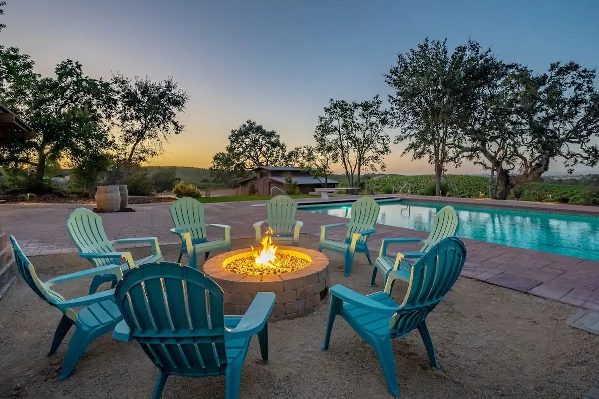 Gas fire pit with Adirondack chairs at sunset under oak trees