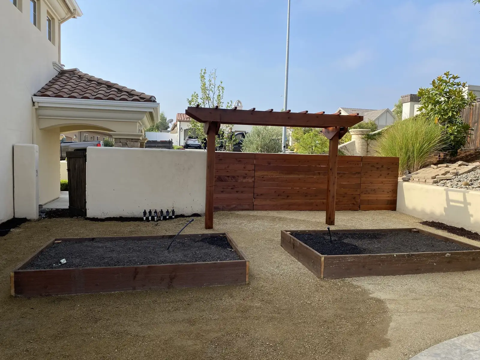 Raised garden beds under a timber pergola beside a horizontal fence