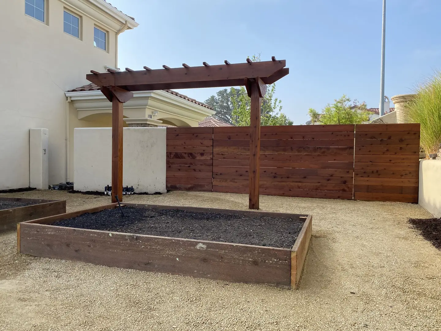 Redwood raised garden bed under a timber pergola beside a horizontal fence