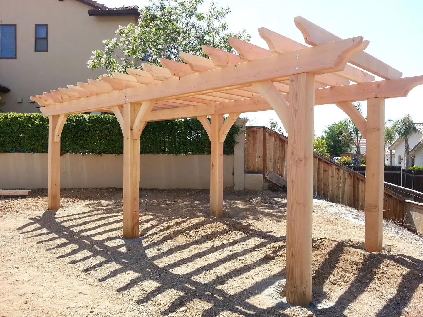 New rough-sawn timber pergola standing over a freshly graded dirt yard beside a wood fence