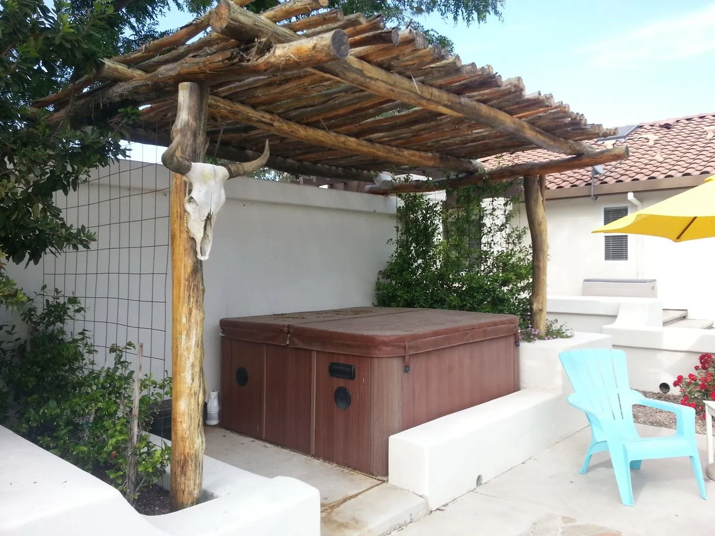 Rustic wood pole pergola shading a hot tub that sits on a concrete patio pad