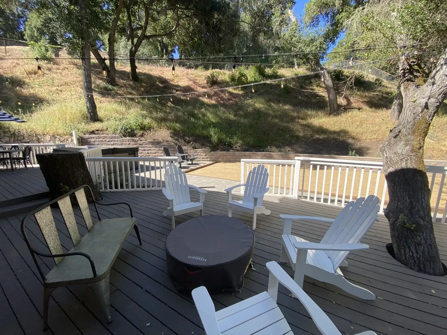 Wood deck with a fire table and Adirondack chairs among oaks