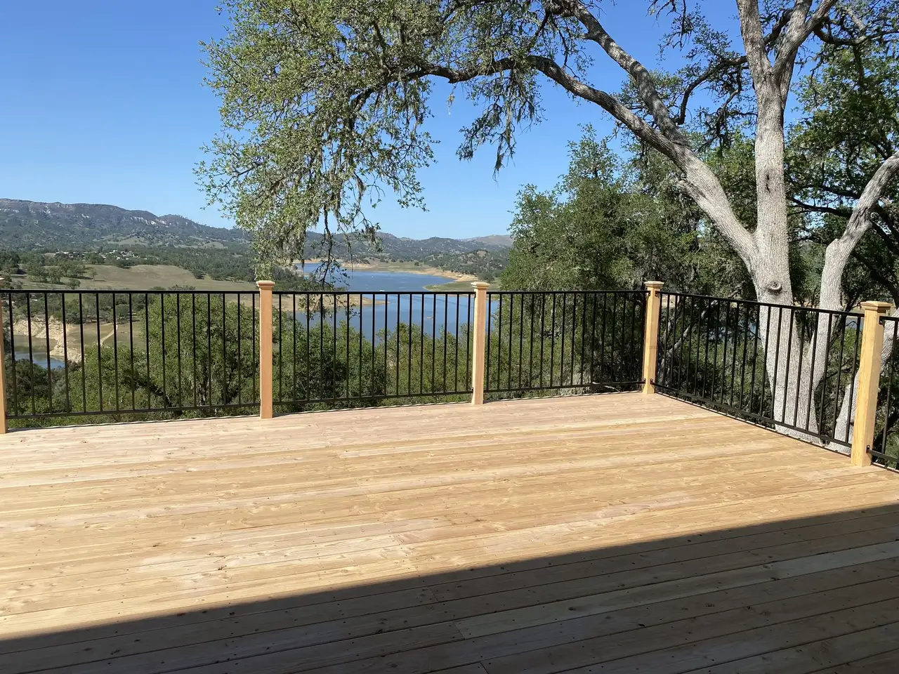 Wood deck with metal railing overlooking a lake and oak hills