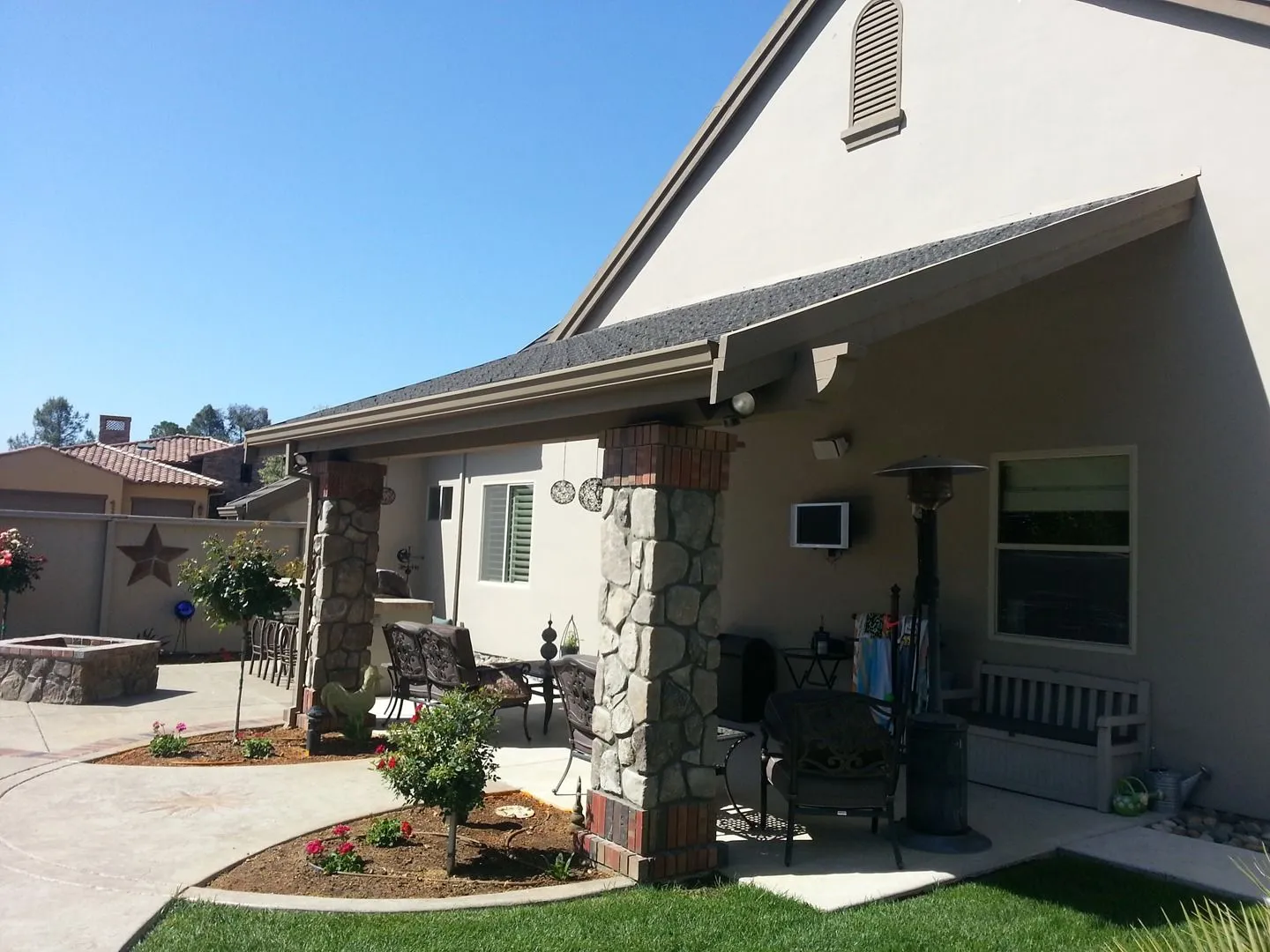 Covered patio with stone columns beside a lawn and planting bed