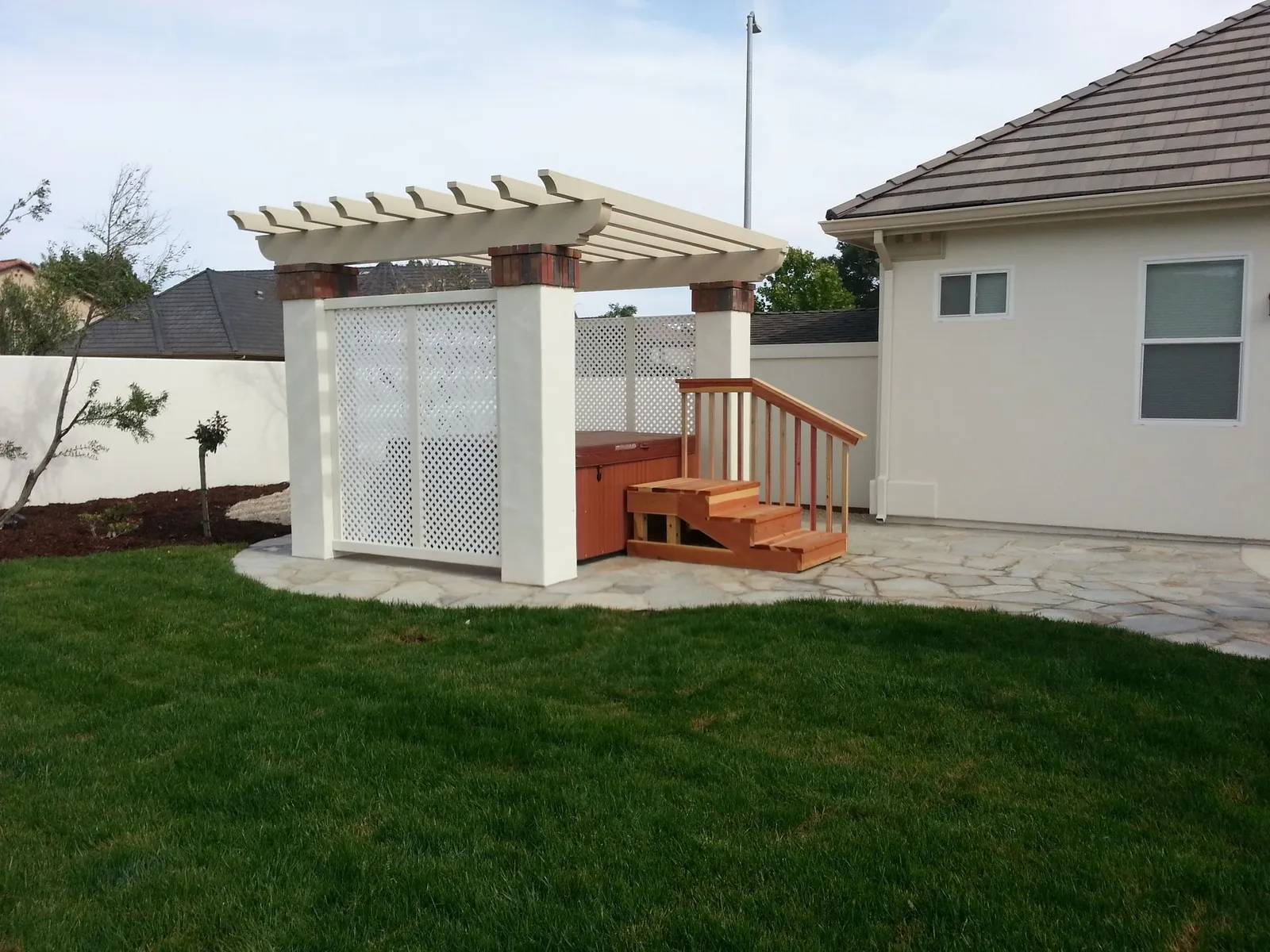 Hot tub under a pergola enclosure beside flagstone and lawn