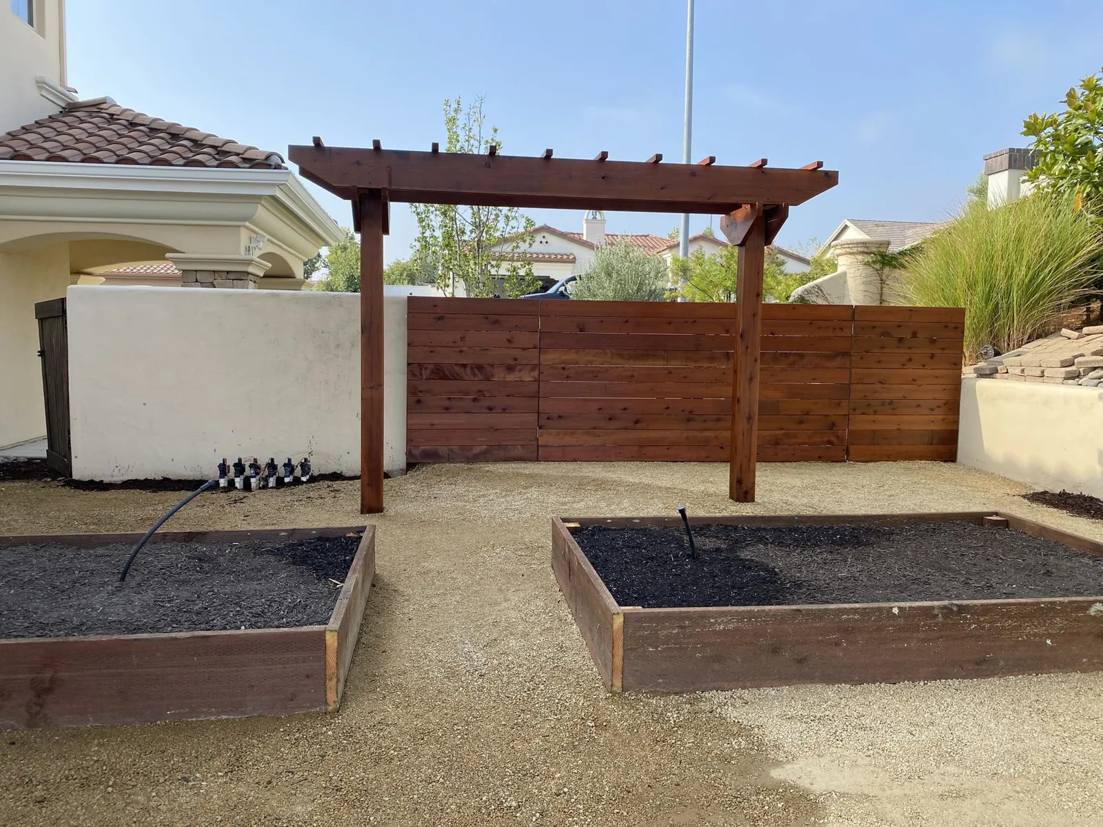 Two redwood raised planting beds on a level yard in front of a timber pergola and a horizontal wood fence