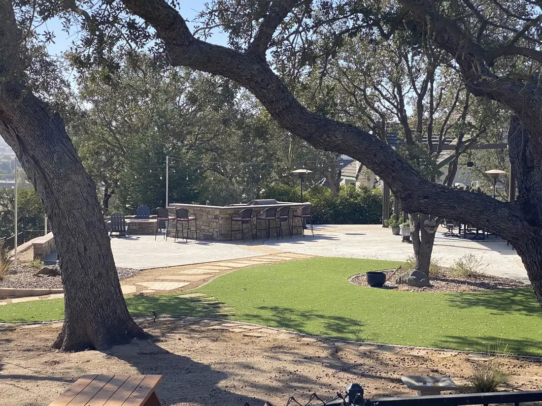 Turf beside an outdoor kitchen and seat wall under oaks