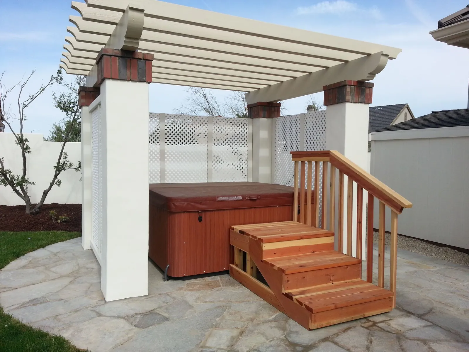 White pergola over a hot tub with redwood steps on a paver patio