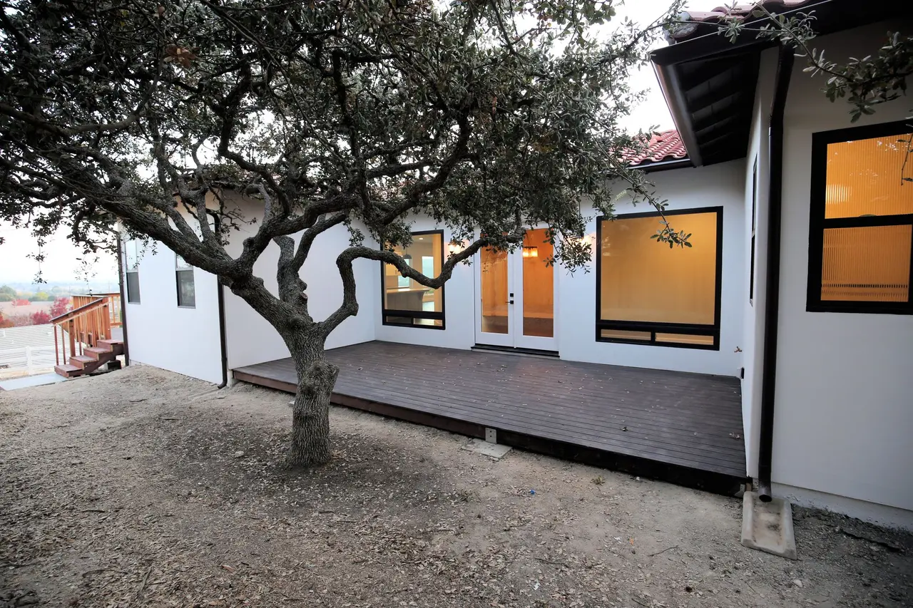 Wood deck beneath an oak beside a modern white house