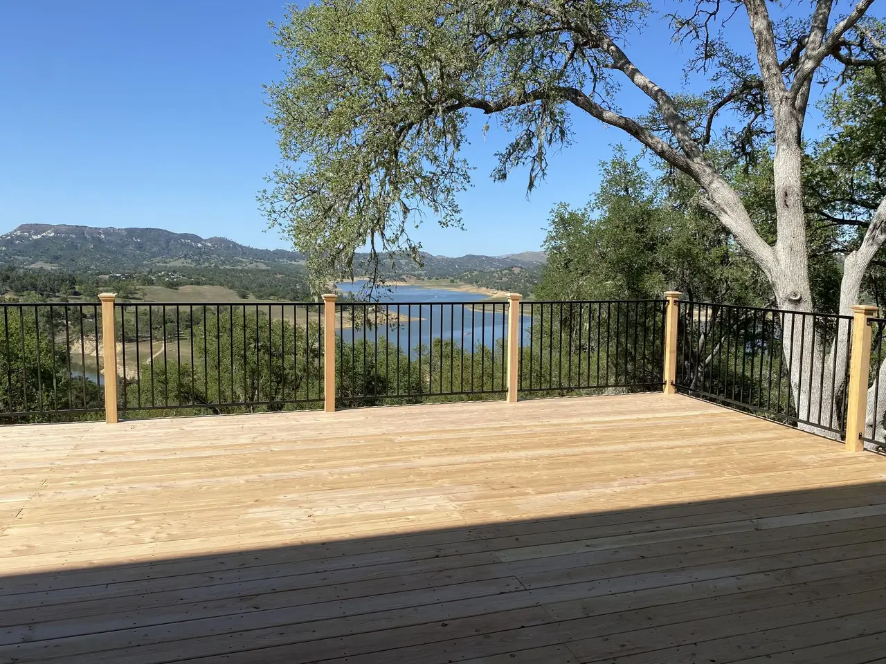 Wide wood deck with railing overlooking water and hills