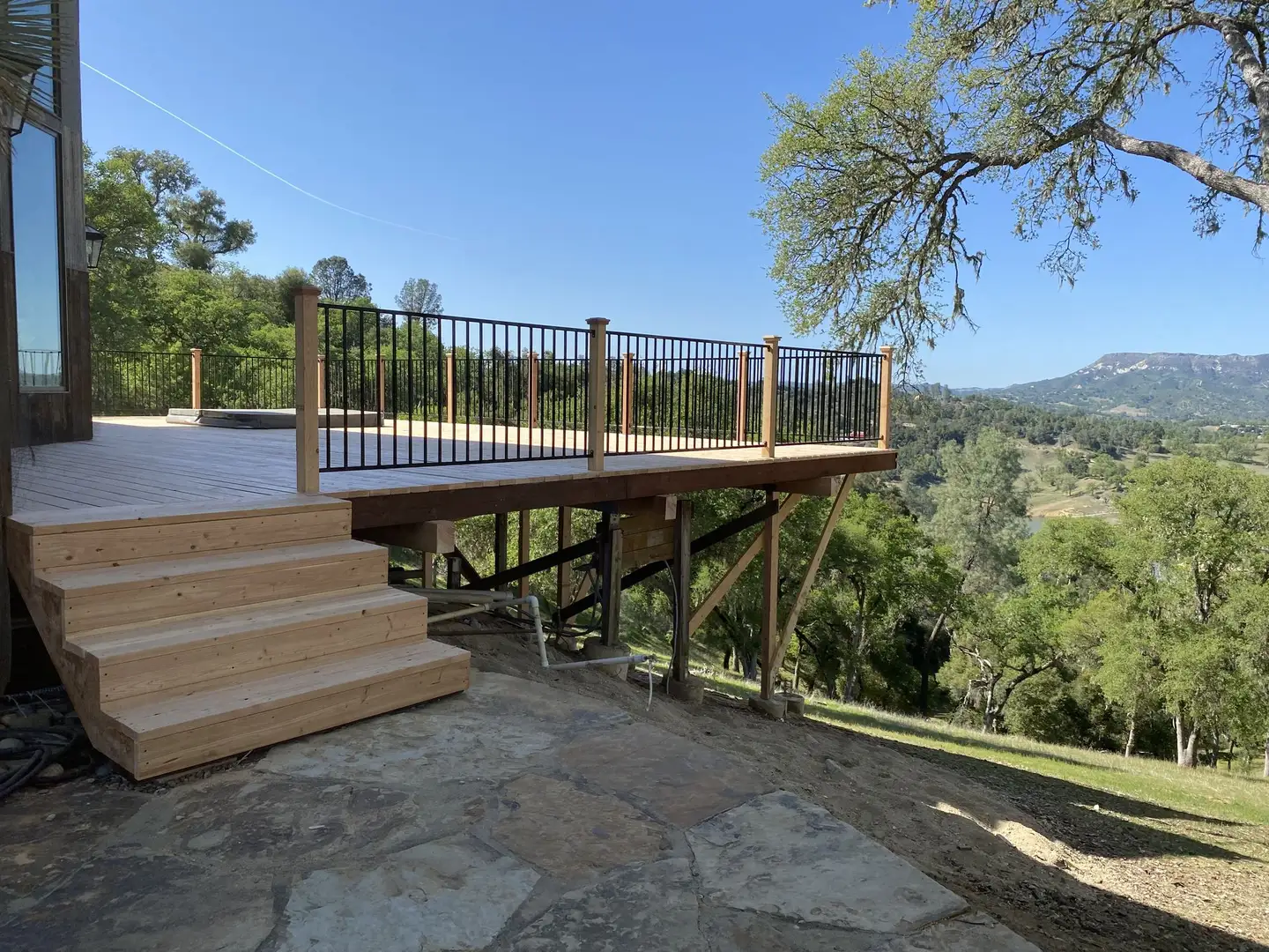 Wood deck stairs leading down to a flagstone patio on a slope